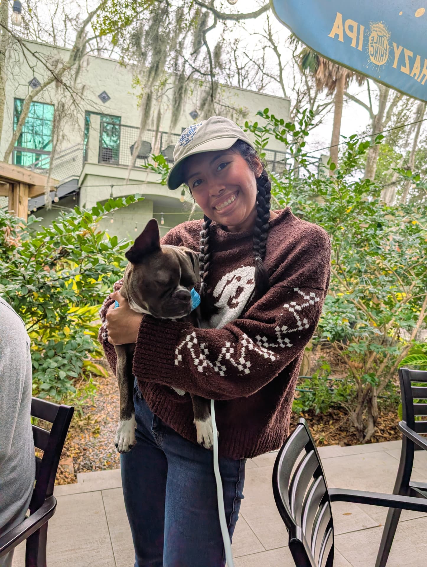Kathryn smiling in a baseball cap, holding her dog at an outdoor gathering